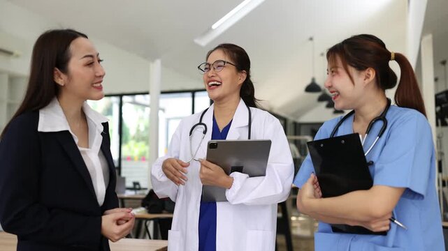 A group of Asian female healthcare professionals, including a doctor and a nurse, having a friendly conversation and smiling with a businesswoman in a modern office or clinic setting.