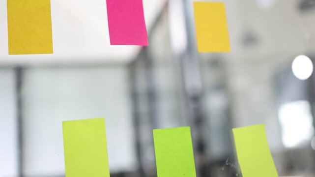 Colorful adhesive sticky notes attached to a glass office wall, representing business brainstorming, project planning, agile workflow, and creative teamwork in a modern workspace.