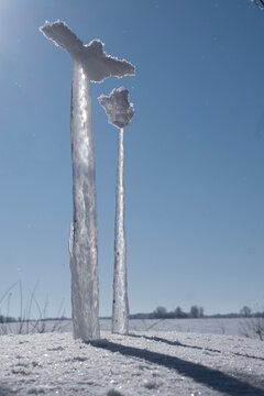 Thick ice formations and icicles frozen on vertical poles in a winter landscape