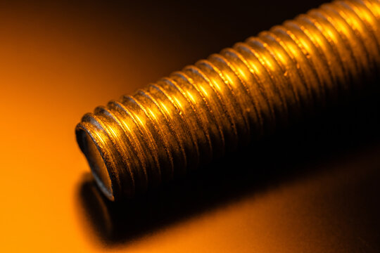 Metal threaded rod macro with warm orange light highlighting grooves, industrial texture, and engineering detail