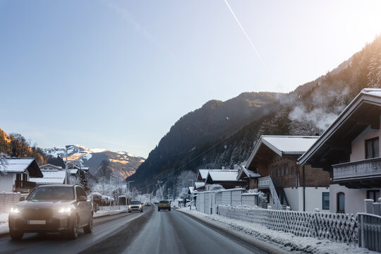 Scenic alpine village resort in Austria gondola cablecar above snowy road car parking lots trees mountain valley scenery under clear blue winter sky. Scene winter tourism destination