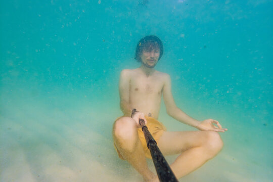 Man meditating underwater at the bottom of the sea in calm blue water. Mindfulness, wellness, inner peace, mental health and spiritual balance concept in nature