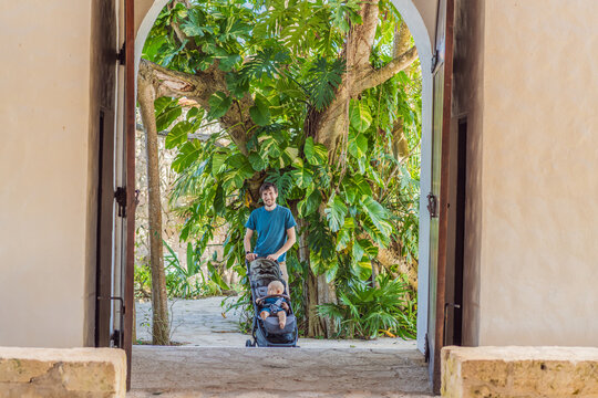 Dad walks with an infant stroller through dense tropical greenery, showing family travel, fatherhood, eco park visit and vacation routine concept