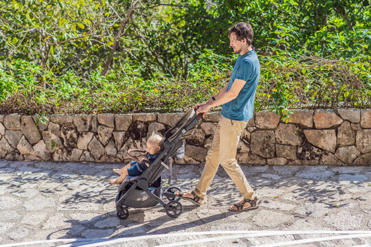 Dad walks with an infant stroller through dense tropical greenery, showing family travel, fatherhood, eco park visit and vacation routine concept