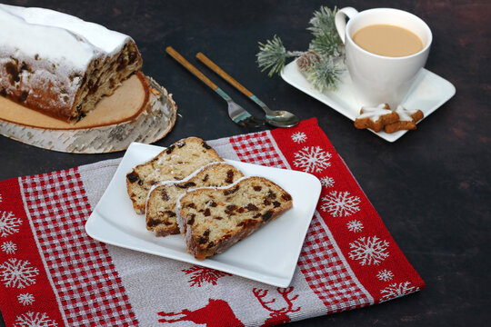 Slices of traditional Christmas stollen on a white plate, served with coffee and cinnamon stars on a festive red table runner.