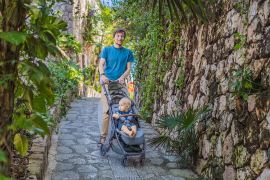 Dad walks with an infant stroller through dense tropical greenery, showing family travel, fatherhood, eco park visit and vacation routine concept