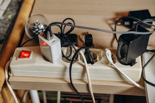 Overloaded Power Strip With Multiple Chargers and Tangled Cables on Wooden Desk Showing Electrical Clutter