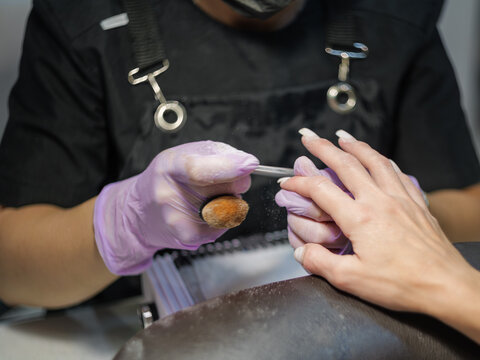 A horizontal shot of a salon master in protective gloves filing and shaping nails for a client during a beauty treatment.   