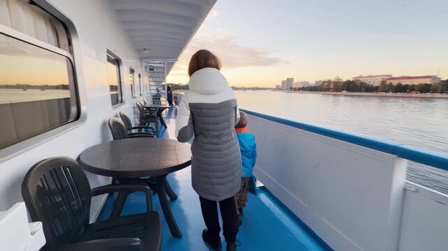 A mother and son look out at the cityscape from a cruise ship deck along the Neva River. They feel peaceful and joyful enjoying the journey together. The calm river view brings happy moments.