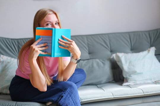 Female reader embracing colorful books on a couch, illustrating love of literature, knowledge and cozy home leisure.