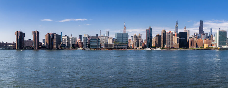 Midtown Manhattan skyline stretches across the East River waterfront on a clear day, revealing towers and the United Nations headquarters along the urban shoreline in New York.