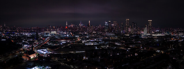 Fototapeta premium Aerial view displays the illuminated skyline of Manhattan and surrounding boroughs in New York City during nighttime, showing glowing streets and architecture.