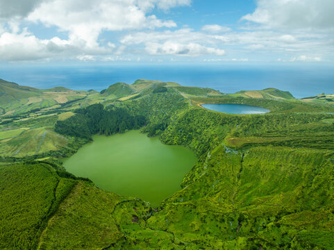 Aerial view of the spectacular volcanic crater lakes Lagoa Rasa and Lagoa Funda on Flores Island, Azores, Portugal. High viewpoint over lush green calderas with the Atlantic Ocean on the horizon