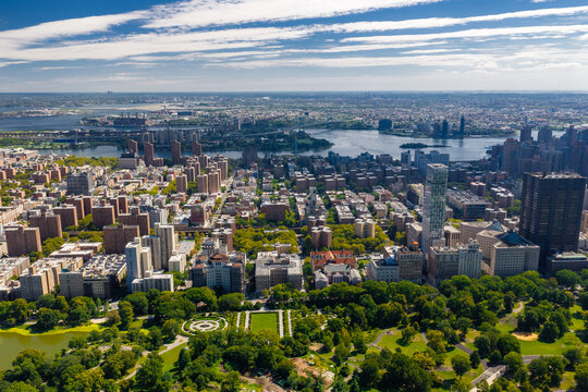 Aerial perspective looking northeast across Central Park Conservatory Garden, East Harlem, the East River, and bridges under a partly cloudy summer sky in New York City.
