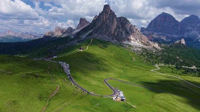 Aerial drone backward tracking shot of the Ra Gusela mountain peak and winding alpine road at Passo Giau in the Dolomites, Italy