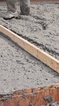 Worker spreads wet concrete for foundation on construction site with wood framing in place.