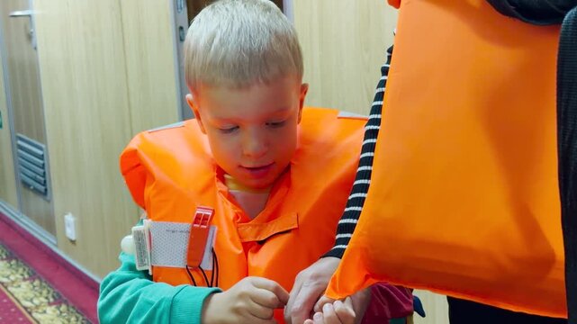 A young boy inspects his orange lifejacket in a cruise ship corridor along the Neva River, Saint Petersburg. He feels curious and focused. The safety practice brings a reassuring and safe mood.
