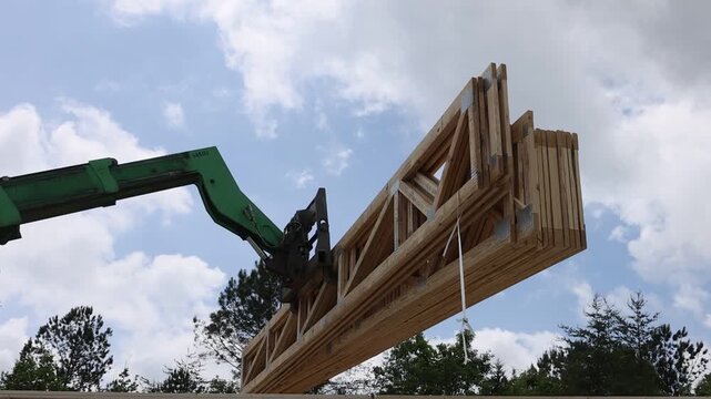 Workers are lifting large wooden trusses with telehandler at construction site is busy with activity.