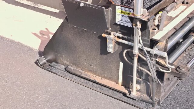 Large paving machine works on road, laying down fresh asphalt at construction site