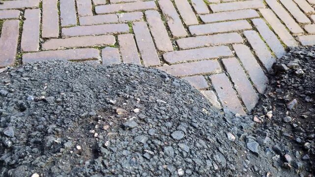 fresh black asphalt pile, road construction material, paving stones, herringbone brick pattern, construction site, infrastructure development, engineering project, asphalt texture