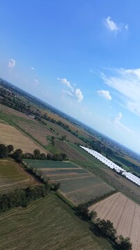 Rural Landscape from Above: An aerial perspective reveals a patchwork of agricultural fields, a greenhouse, and a clear blue sky dotted with fluffy clouds, showcasing the beauty of the countryside.