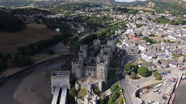 Camera pulling back from high angle above historic medieval fortress, revealing tidal river, road bridge, and coastal town