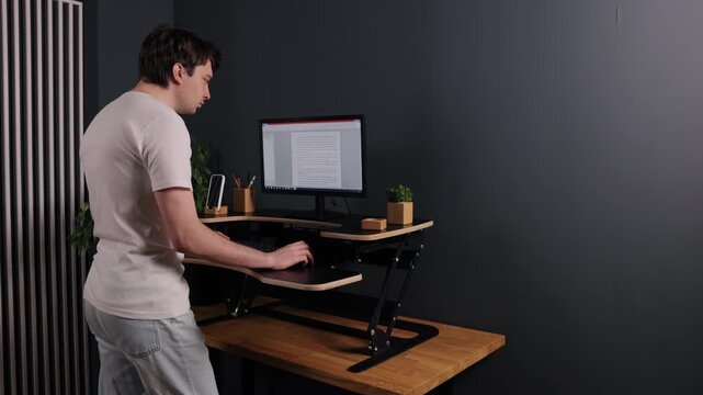 Digital writing, typing document, man desk. From rear view, man in white shirt is typing on computer at standing desk with document on screen.