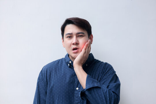 close up young asian man frown and use hand to massage on cheek after feeling pain or hurt from tmj muscle symptom at home for un healthy lifestyle and treatment concept