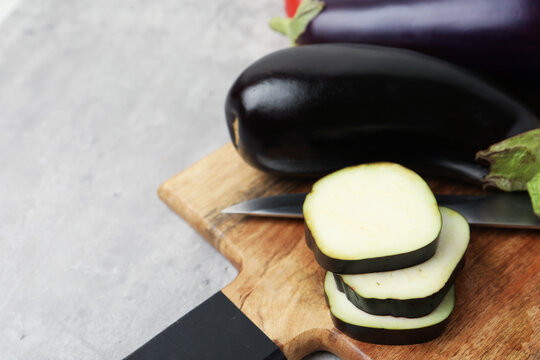 Fresh raw eggplants, board and knife on light grey table, closeup. Space for text