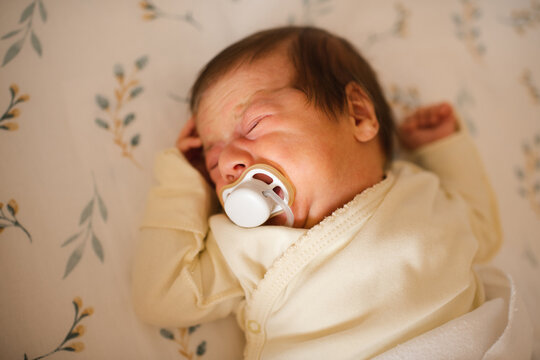Crying infant baby sleeping with colic pain in crib with pacifier close up. Childhood.