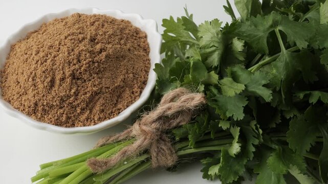 Fresh coriander leaves and ground powder on a white background