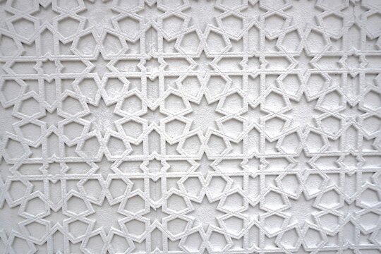 Intricate white geometric pattern with repeating Islamic star and polygon motifs creating a textured surface