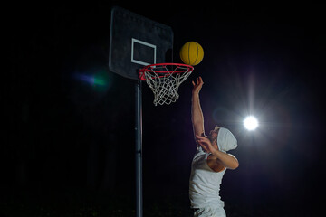 A man performs a slam dunk on a basketball court at night under the glare of bright outdoor lights © nazariykarkhut