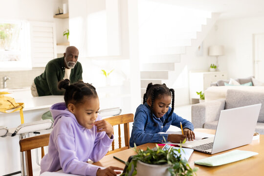 African American family supervising two youth females doing homework at kitchen table with laptop