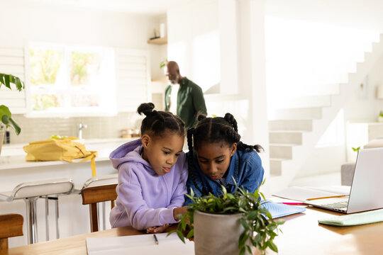 African family father supervising while two youth females studying at wood dining table with laptop