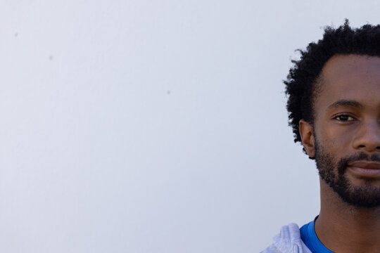 African American man posing on right against pale wall wearing gray hoodie, blue shirt, copy space