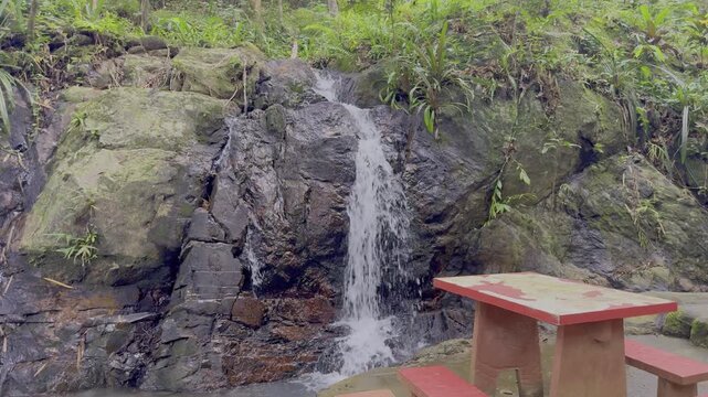 Kathu Dam waterfall water gently flowing down the rocks surrounded by lush green trees flowers and tables Patong on the Island of Phuket Thailand