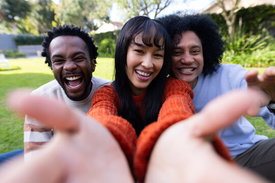 Friends laughing and reaching with outstretched hands on manicured lawn showing orange sweater