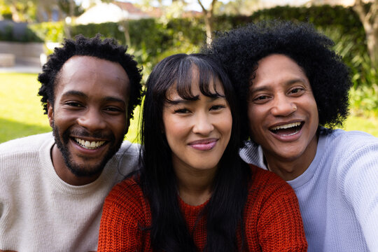 Smiling diverse friends posing on sunlit lawn in backyard, wearing rust beige blue-gray sweaters