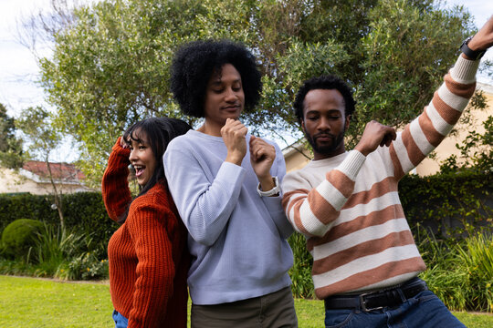 African friends dancing together on grassy lawn wearing knit sweaters and jeans sporting wristwatch