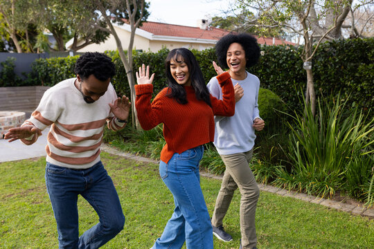 African American friends dancing on lawn wearing sweaters and jeans near hedges and red roof house