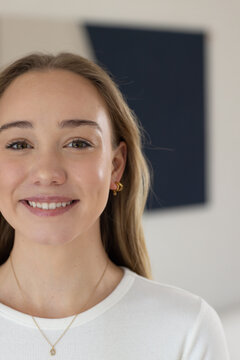 Female adult smiling gently facing camera in studio wearing gold hoops and pendant white ribbed top
