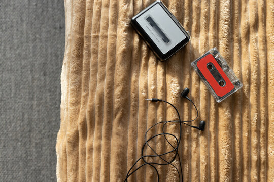 Vintage cassette player and clear cassette are resting with tangled earbuds on ribbed beige throw