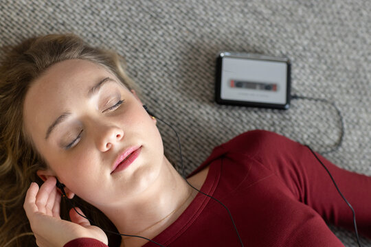 Adult woman lying on carpet at home, wearing maroon top and holding earbuds by cassette player