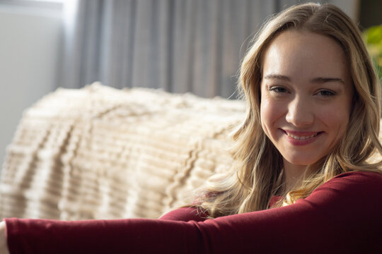 Woman sitting on sofa at home in maroon top, reaching towards camera, copy space