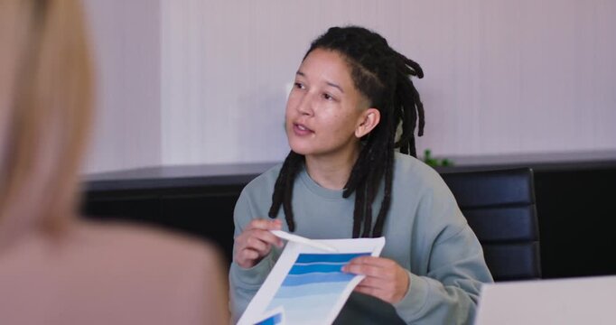 Nonbinary adult of African descent reading chart in meeting looking up explaining with white pen