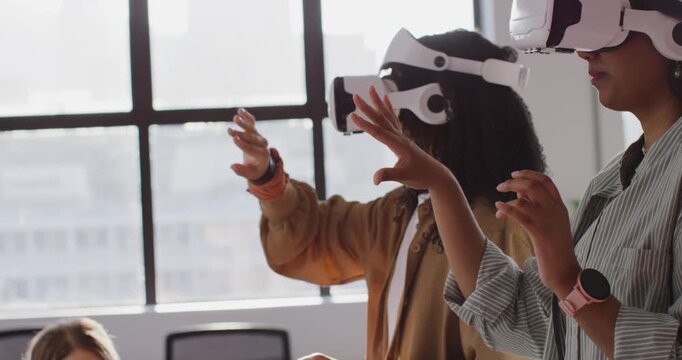Diverse team testing VR woman in jacket white VR headset manipulating interface by window
