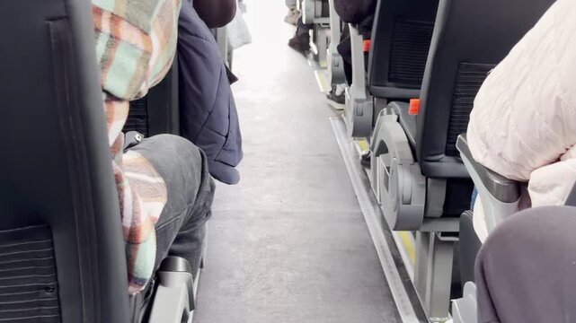 Passengers sit quietly in comfortable seats along a bright bus aisle. People relax on the long trip. The quiet space feels calm and peaceful.