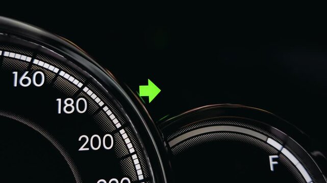 Close-up macro shot of green right turn signal arrow indicator light illuminated on car dashboard speedometer