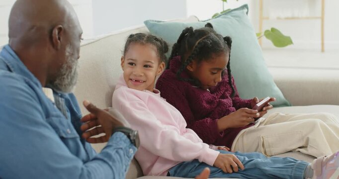 African American man and two girls gesturing on sofa older tapping phone drawing small girl's smile